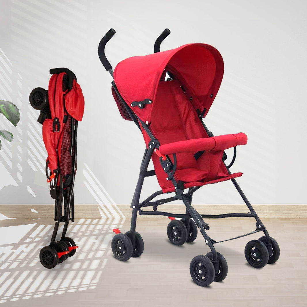 A red and black lightweight baby stroller shown in two positions - folded on the left and fully opened on the right. The stroller features a red fabric seat and canopy with black frame and handles. It has five wheels total with small front wheels and larger rear wheels. The opened stroller shows the full seating area with safety harness straps visible. The stroller is photographed on a light wooden floor against a white wall with natural lighting creating geometric shadows.